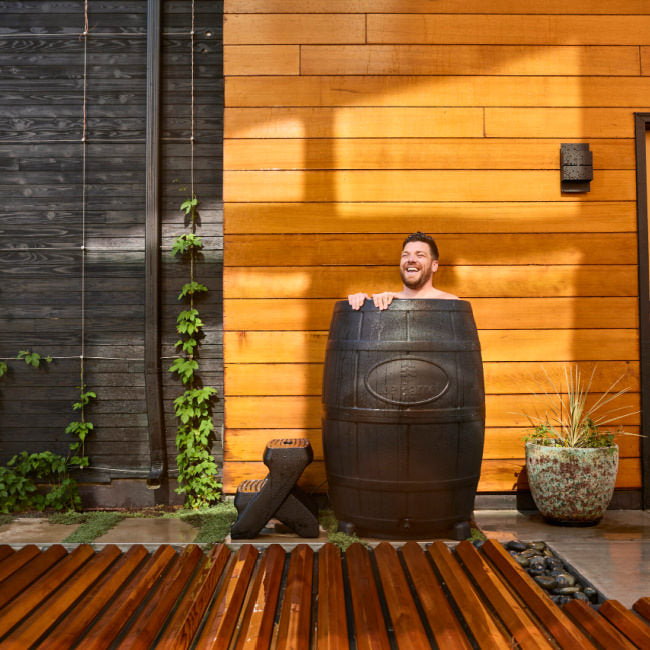 A man smiles as he enjoys a cold plunge ice bath on a summer day