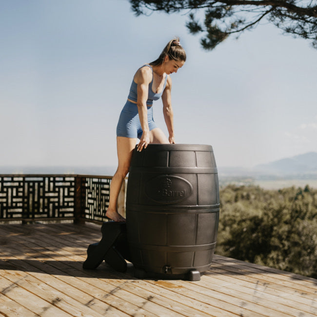 an athletic woman climbs into an ice barrel cold plunge. She is on a balcony on a beautiful summer day.