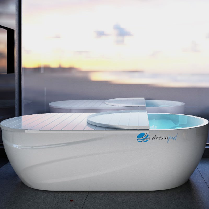 a float tank by dreampod sits in a home against a window with a scent beach view behind.