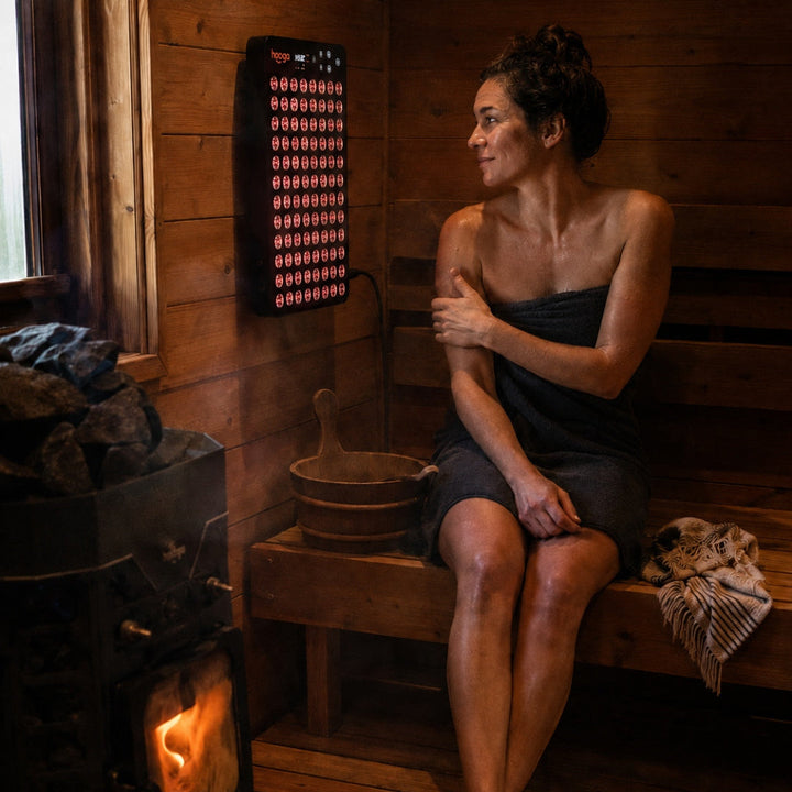 Woman relaxing in a wood-fired sauna next to the Hooga Ember red light panel
