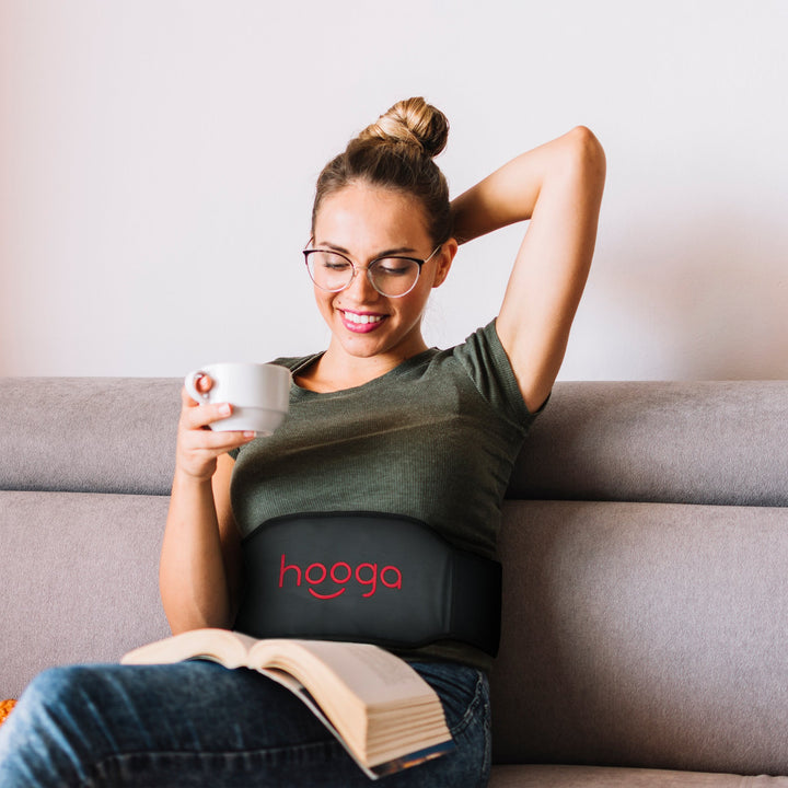Woman reading on a couch with the Hooga PEMF belt wrapped around her waist